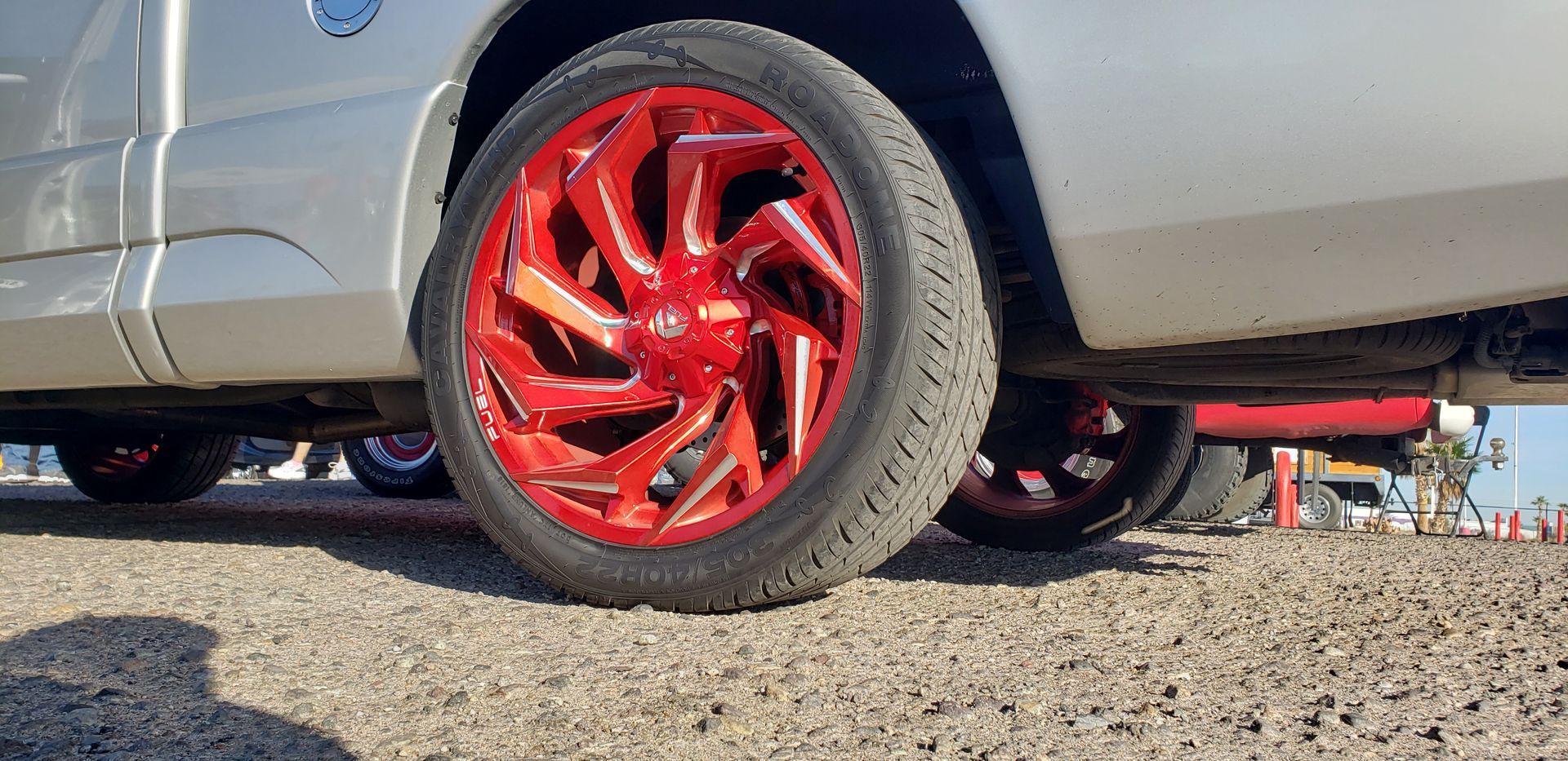 a silver truck with red wheels and tires is parked on a gravel road .