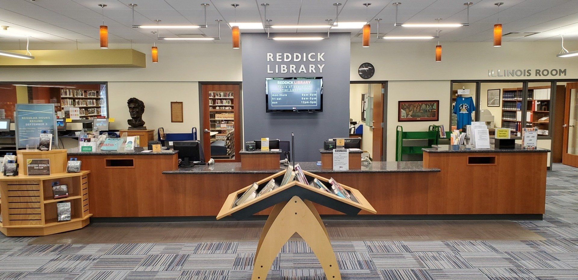 A library with a wooden counter and a tv on the wall.