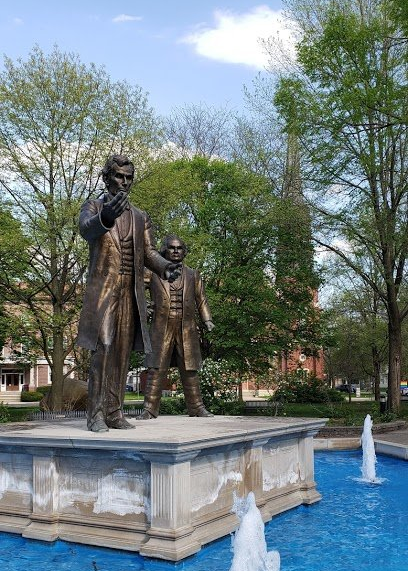A statue of abraham lincoln standing next to a fountain in a park.