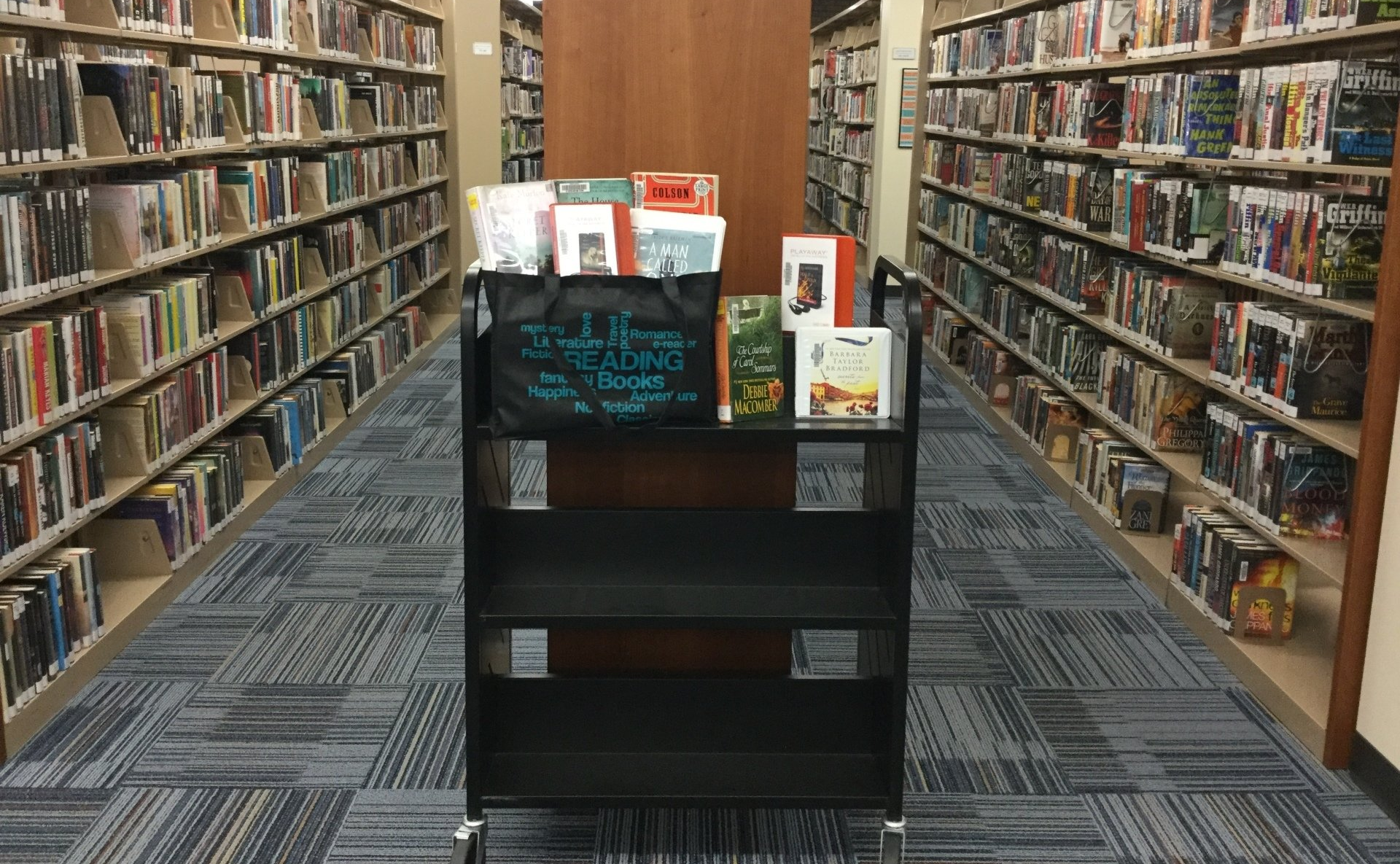 A library filled with lots of books and a cart filled with books.