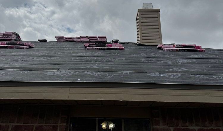 A roof is being installed on a brick house with a chimney.
