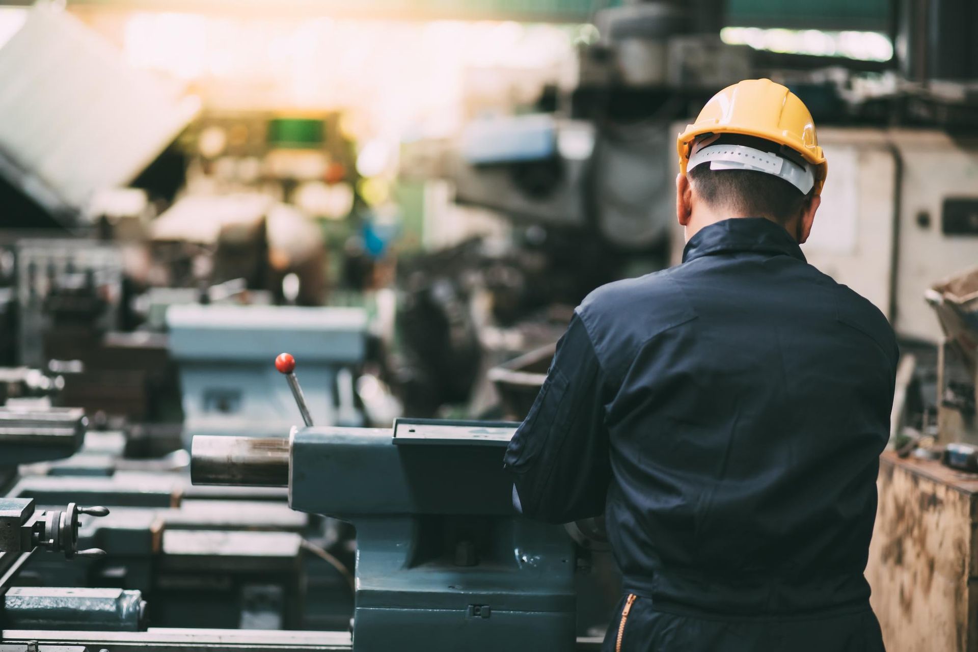 Man in yellow hard hat working in a factory, operating machinery.