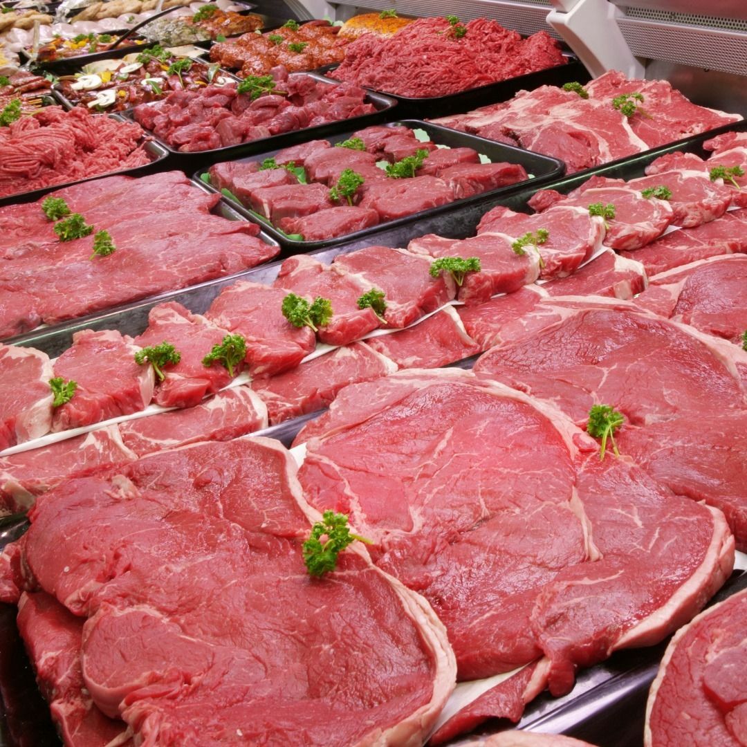 Raw meat cuts displayed in a butcher shop, various sizes and types, red and pink.