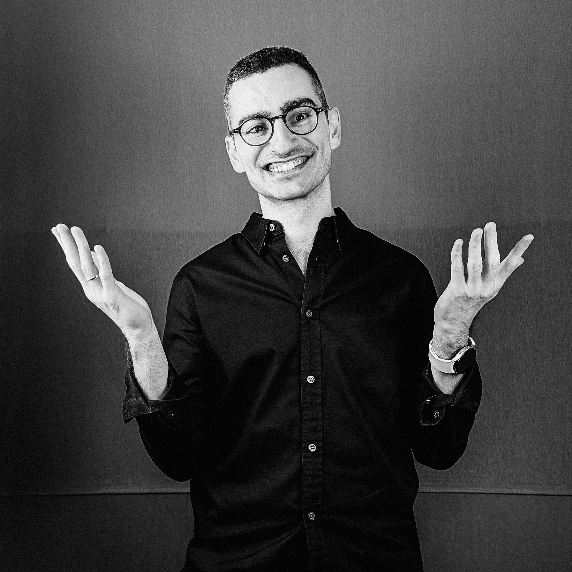 Una fotografía en blanco y negro de un hombre con gafas y una camisa negra.