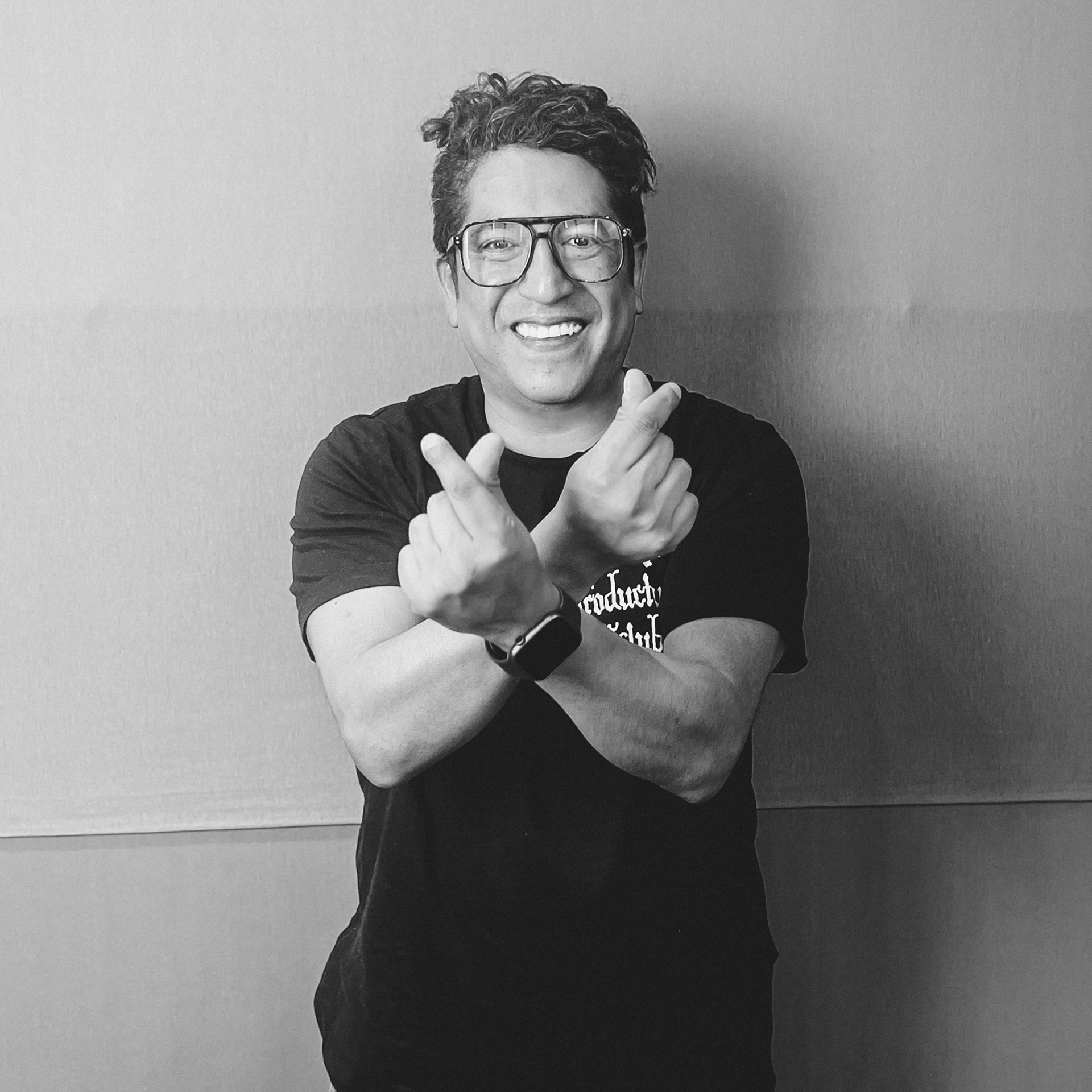 Un hombre que lleva gafas y una camisa negra hace un signo de paz con sus manos.