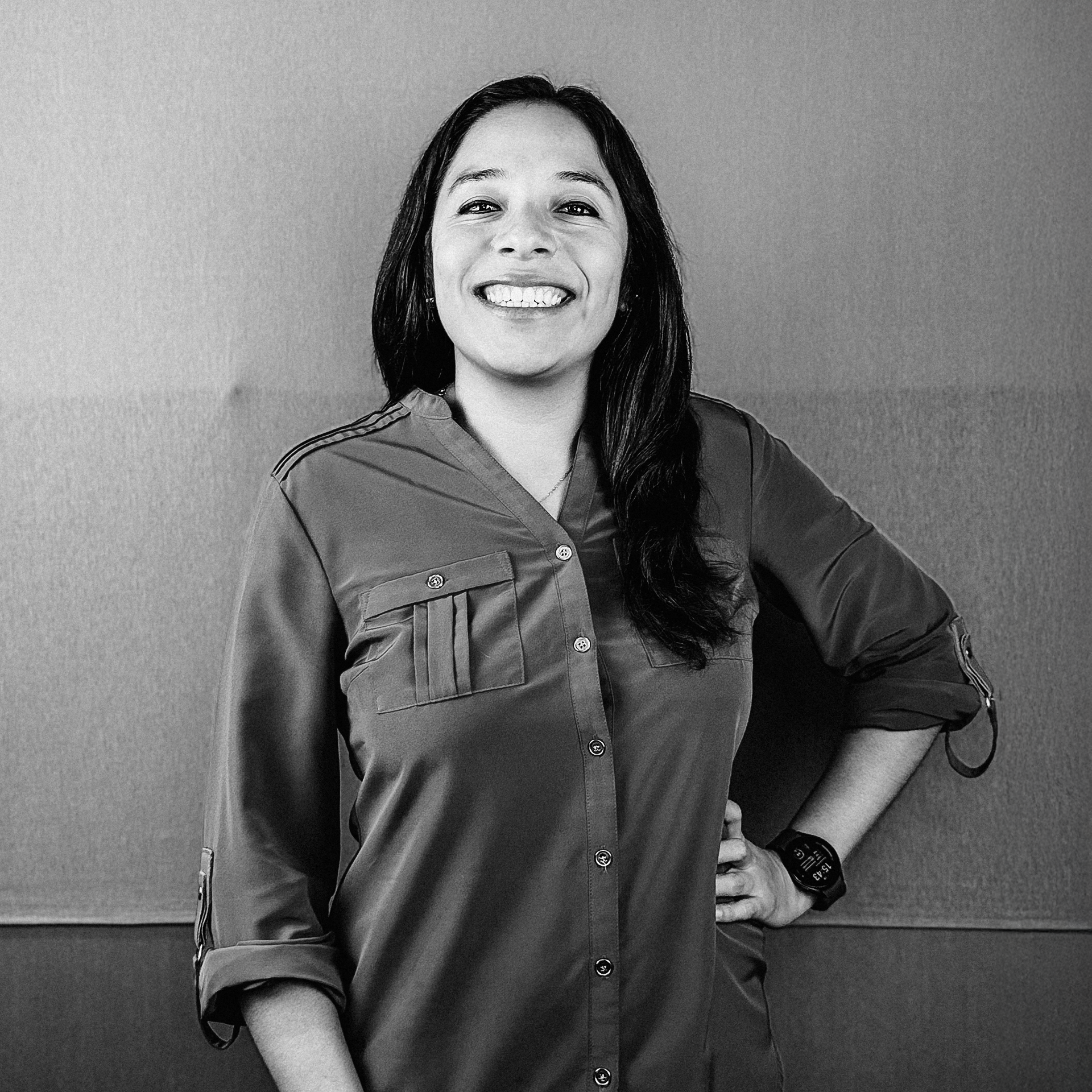 Una mujer sonríe en una foto en blanco y negro mientras está parada frente a una pared.