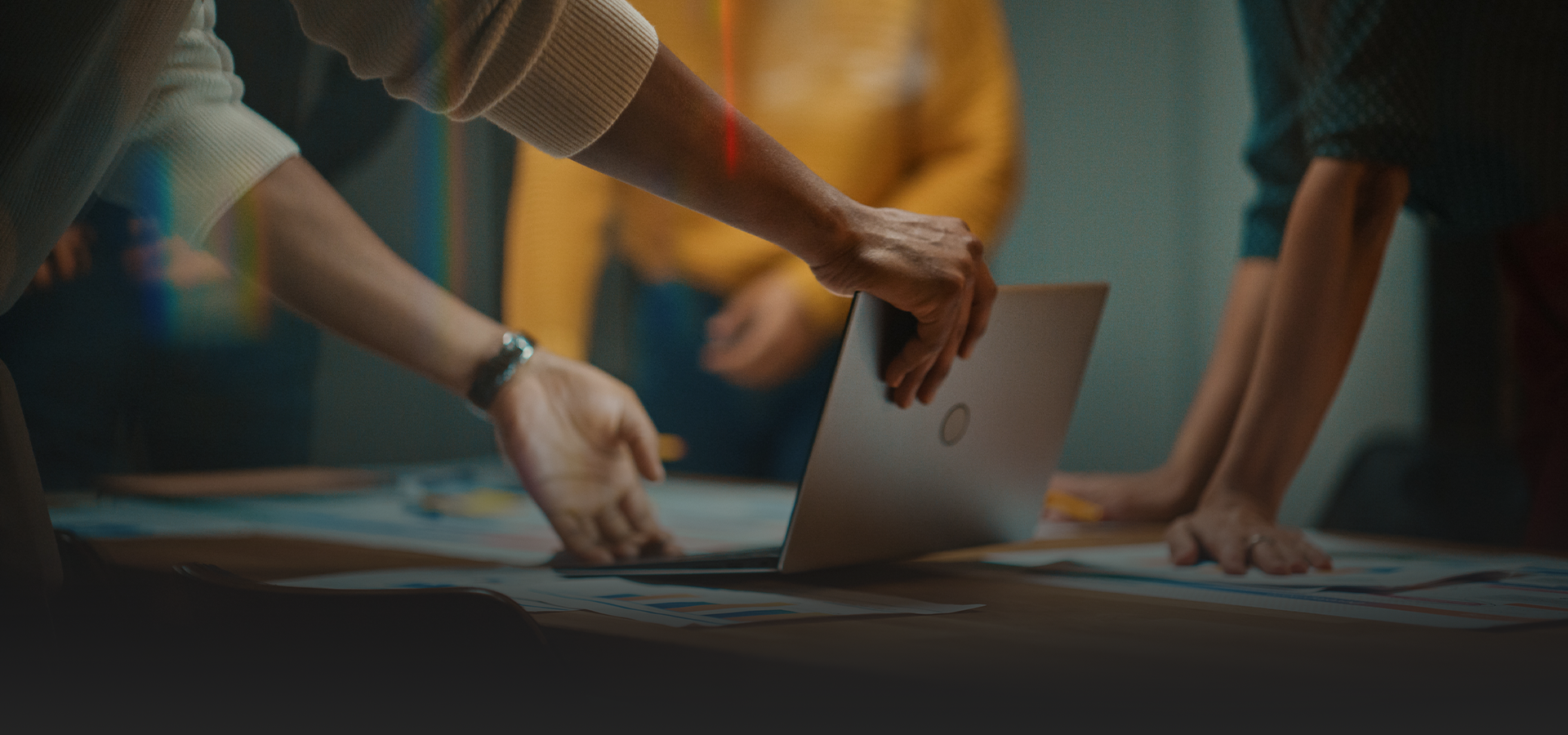 Un grupo de personas están de pie alrededor de una mesa mirando una computadora portátil.