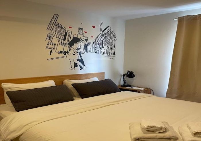Neatly made bed in a modern bedroom with wall art, bedside lamp, and beige curtains