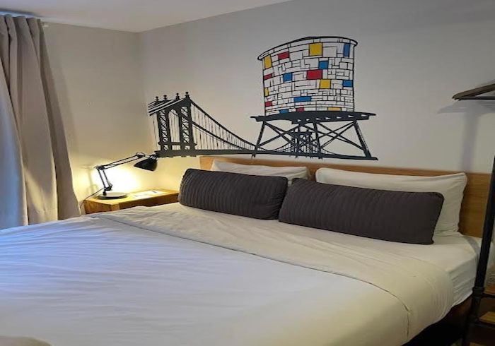 Bedroom with white bedspread, dark pillows, bedside lamp, and bridge-themed wall art above the bed