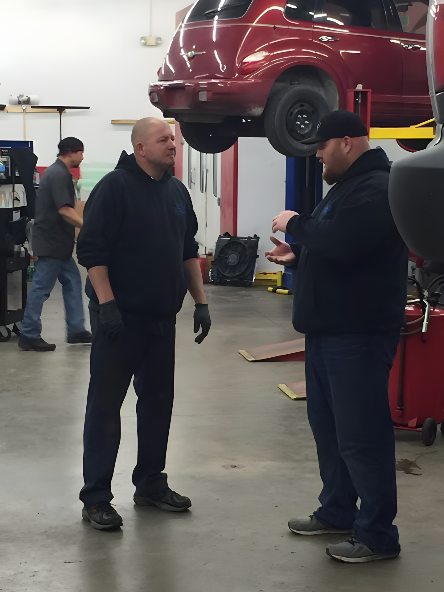 Two men in a garage discussing near a car raised on a lift | C & C Auto