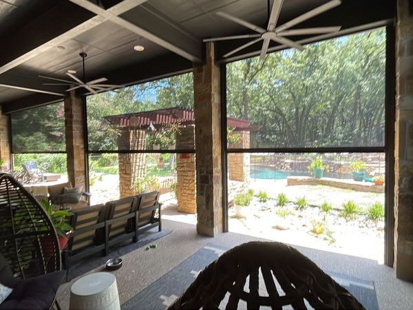 Covered patio with large retractable screens, furniture, and a view of a pool and trees. Black screens are down.