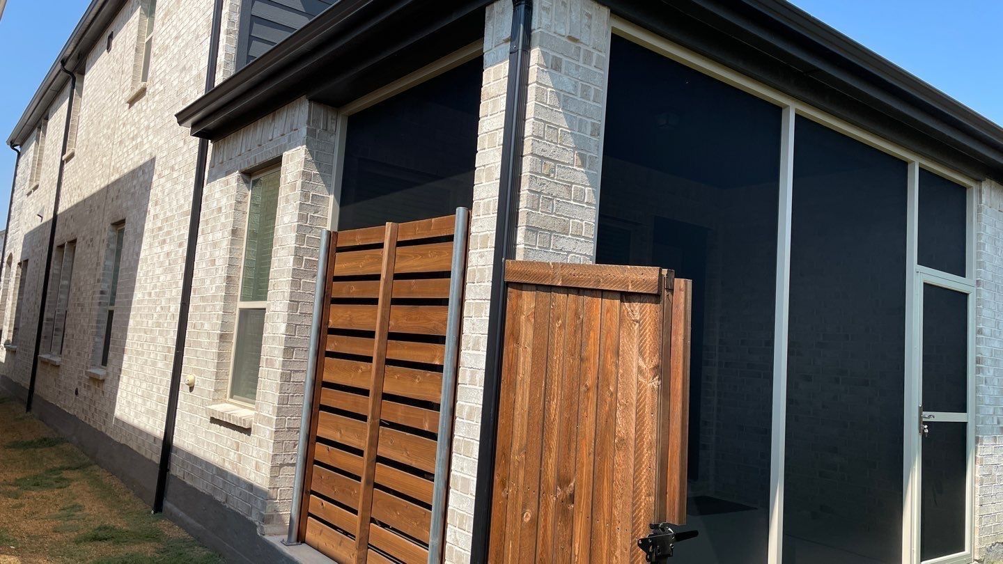 Exterior view of a stucco house with a screened-in porch and wooden fence; bright sunlight.