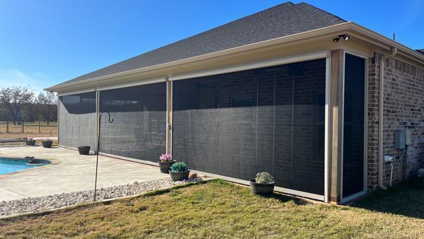 A covered patio with retractable screens, seating, and a view of a pool and trees beyond.