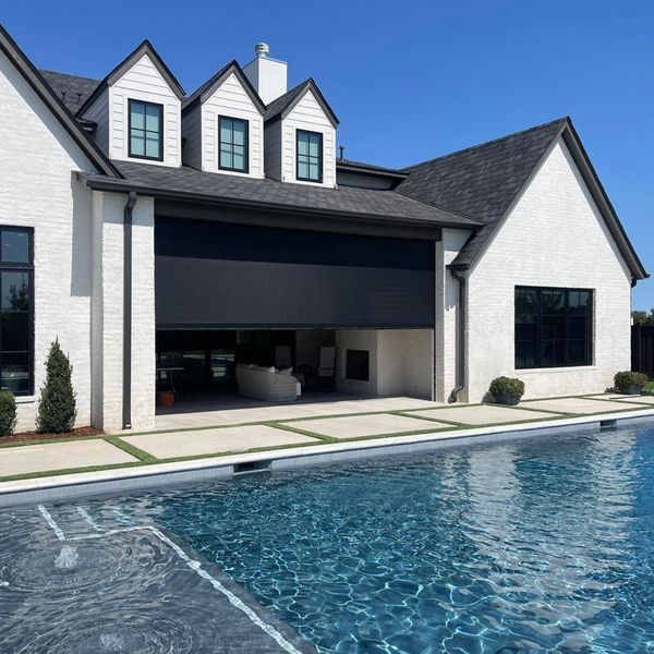 Modern home exterior with a pool and outdoor kitchen area under a covered patio with a television and bar seating.