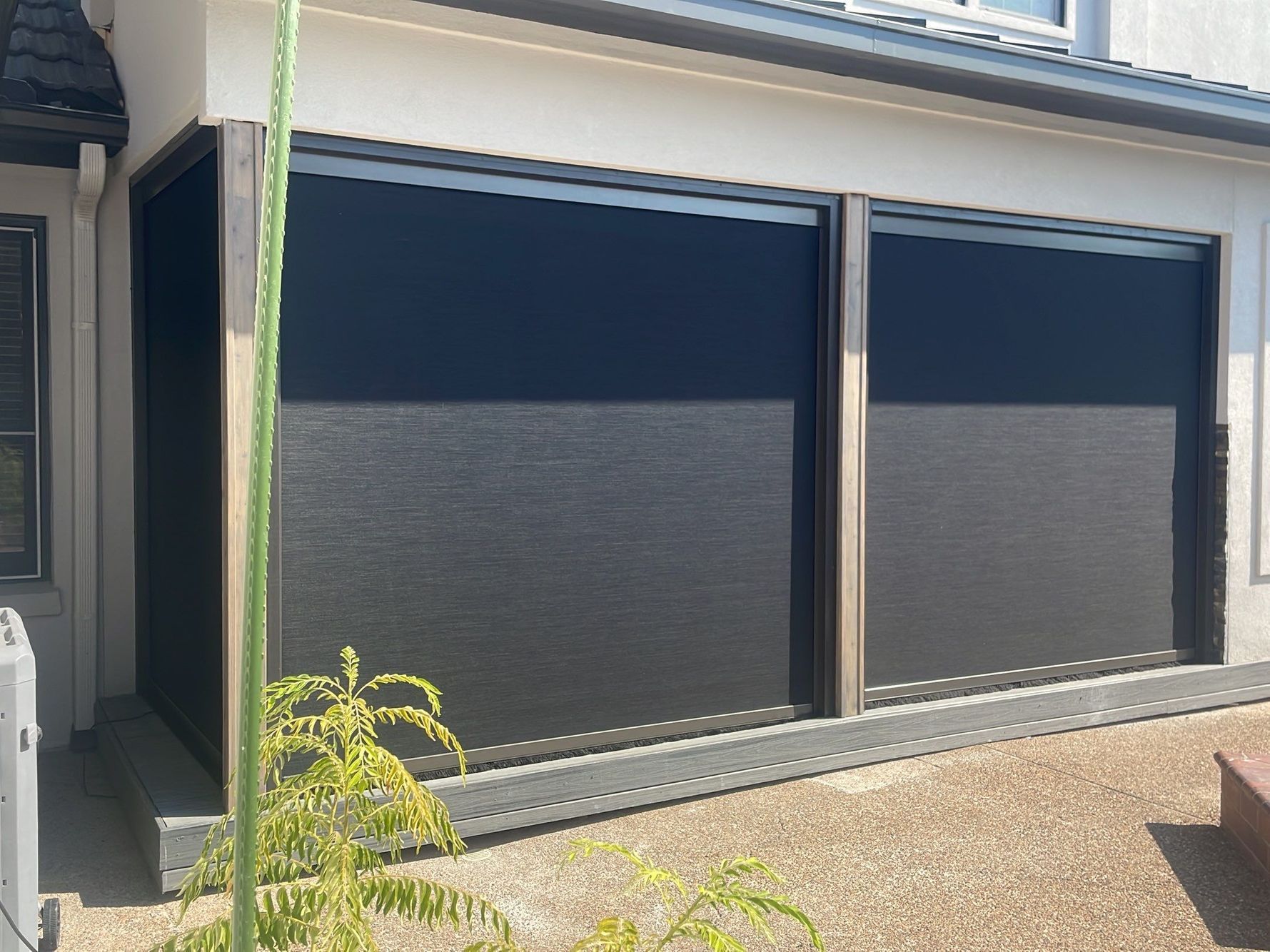 Exterior of a building with two large black window screens pulled down. Beige siding.