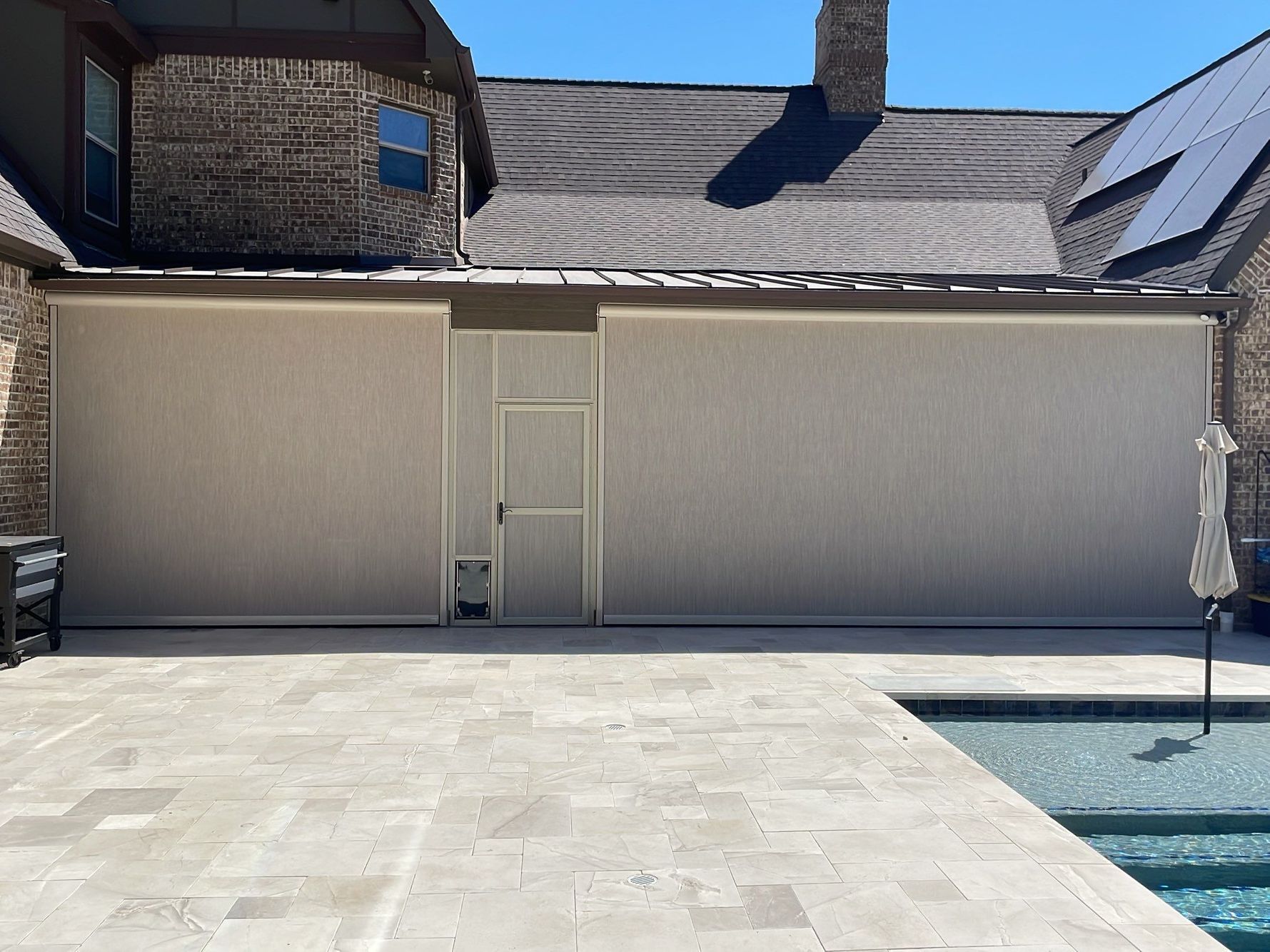 Beige patio sun shades cover a stone house exterior with a pool in the foreground.