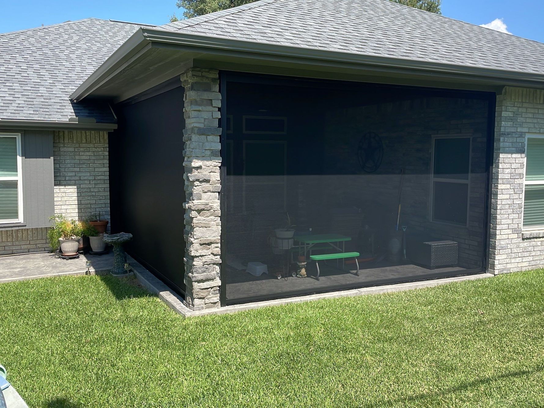 Screened-in porch with black screens, on a brick house with green grass in front.