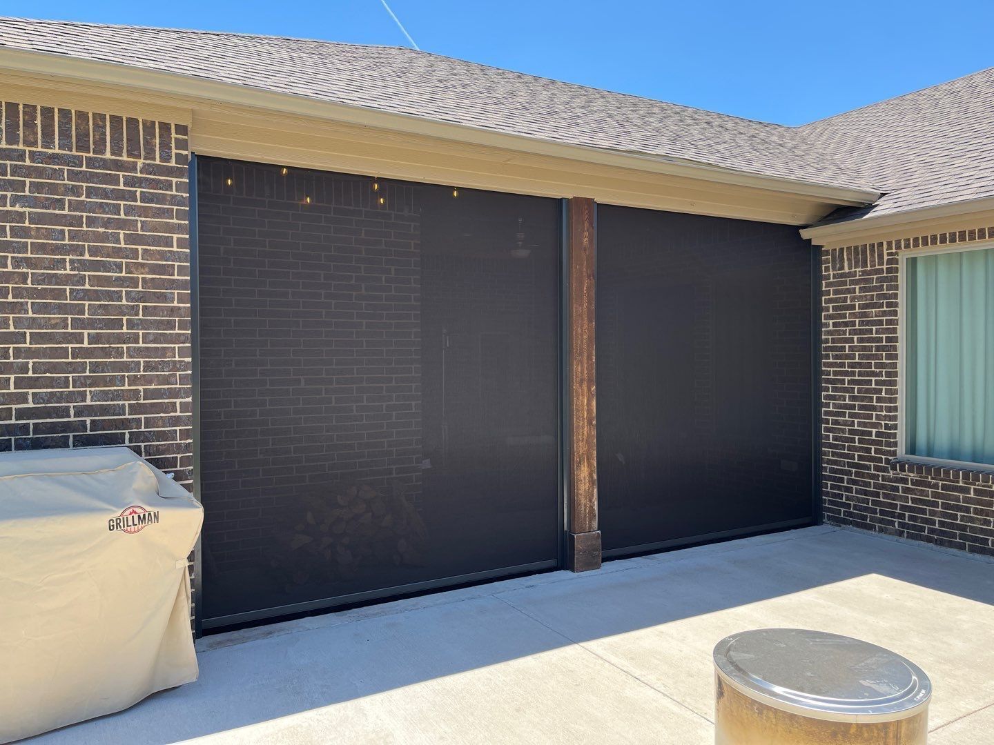 Outdoor patio with two large black screens attached to a brick wall under a roof.