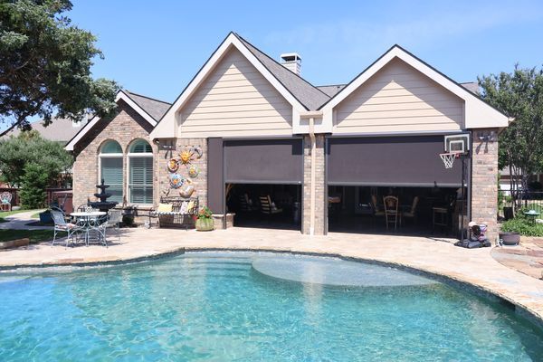 Poolside structure with dark garage doors open. Contains a pool, patio furniture, and basketball hoop.