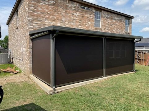 Brown retractable screens enclose a patio attached to a brick house on a grassy lawn.