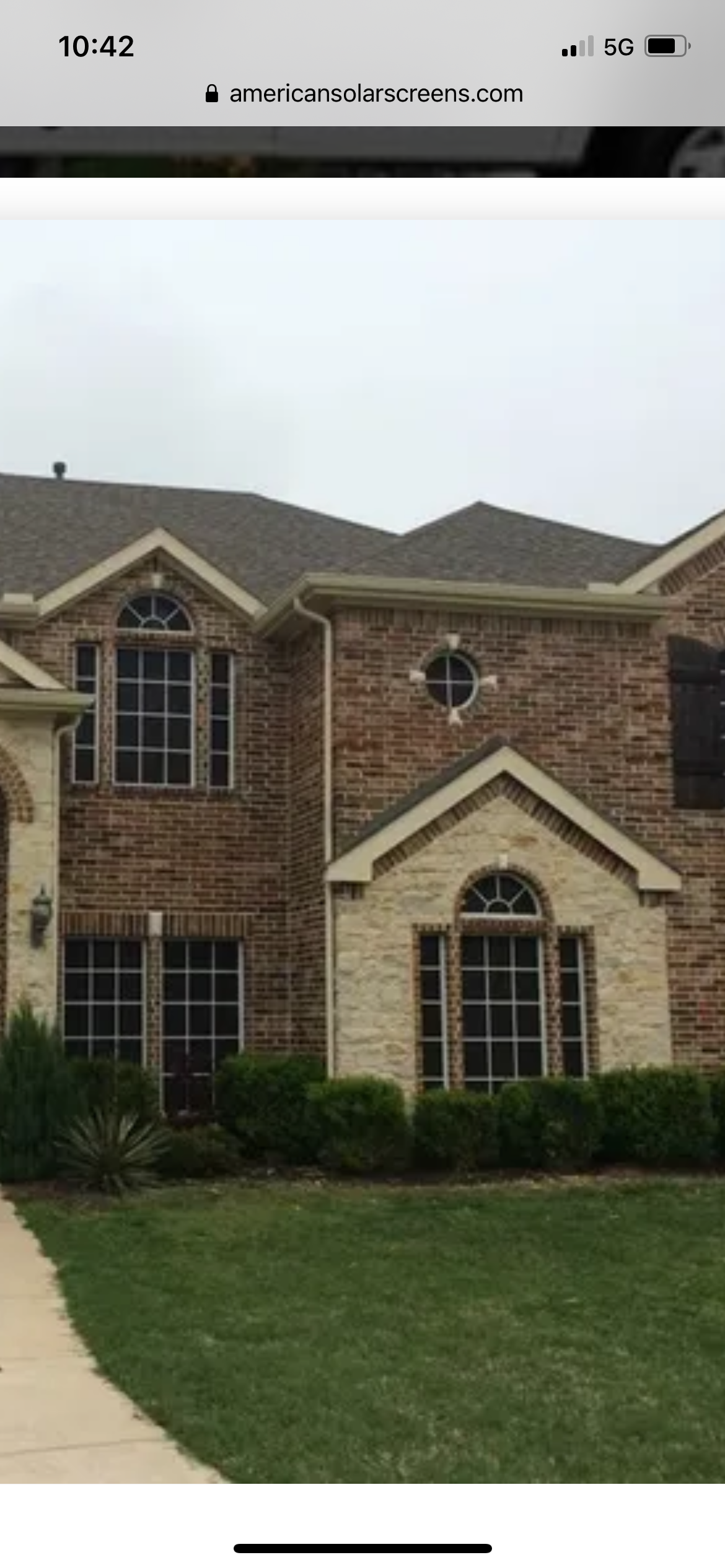 A two-story brick and stone house with a green lawn and a cloudy sky.