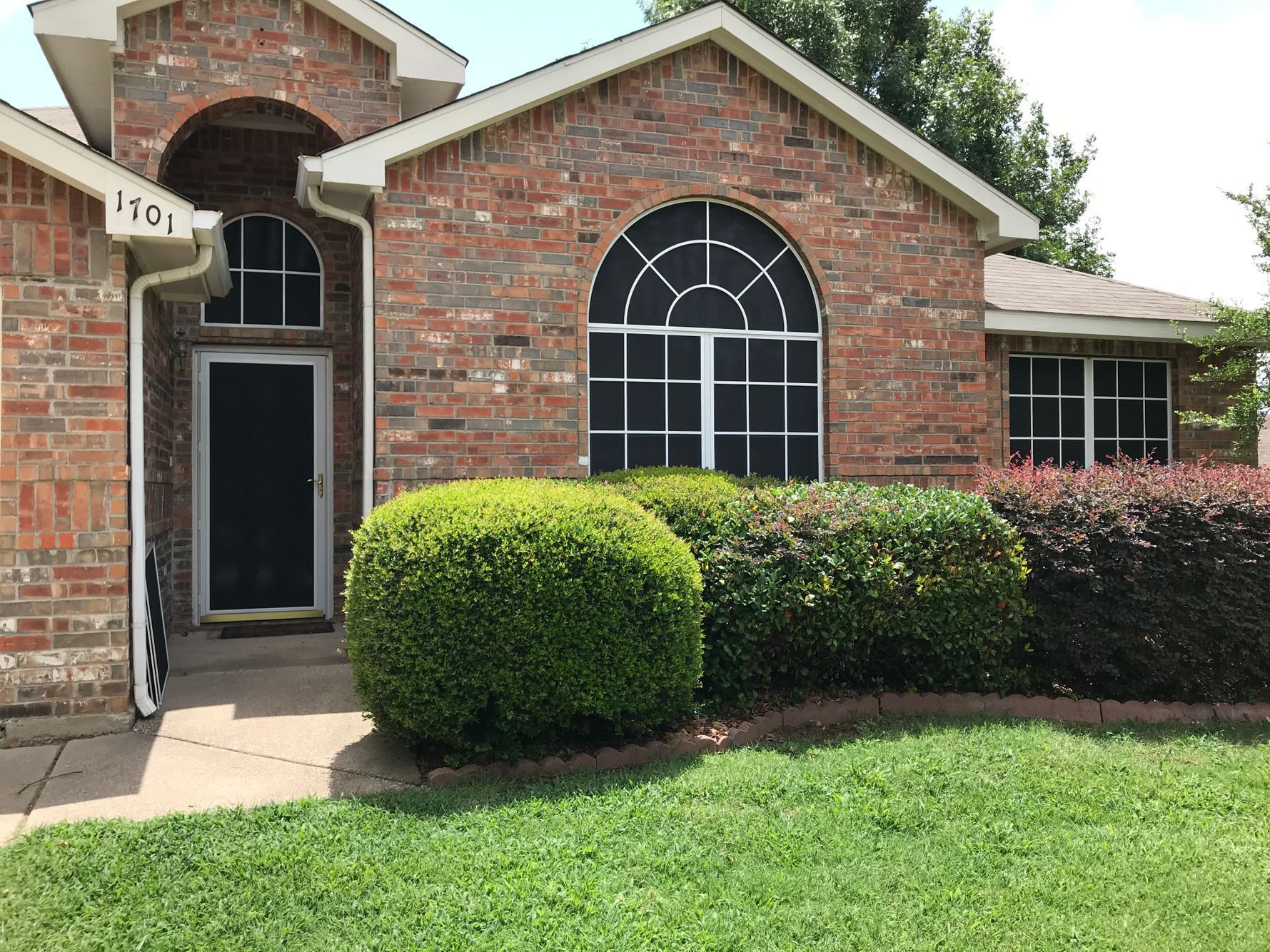 Red brick house with a green lawn and trimmed bushes.