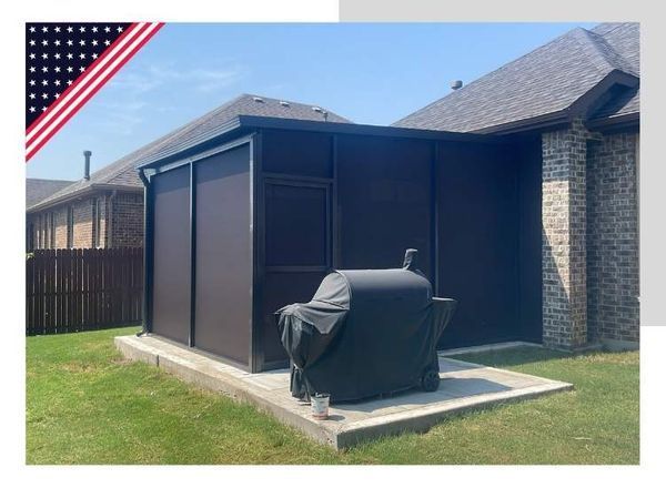 A brown screen room attached to a brick house with a covered grill on the concrete pad. American flag graphic in the top left corner.