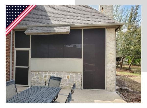 Screened-in outdoor patio with brown screens, stone walls, and a table with chairs. The American flag is visible on the left.