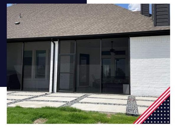 Screened-in patio with black screens, brick wall, and a gray roof. The patio features pavers and green grass.