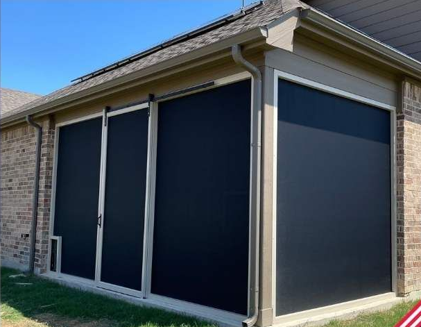 Black retractable screens on a brick patio, against a blue sky.