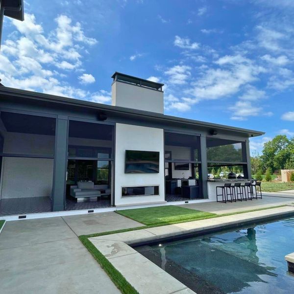 A backyard with a pool in front of a modern house with retractable sun shades. Bright blue sky.