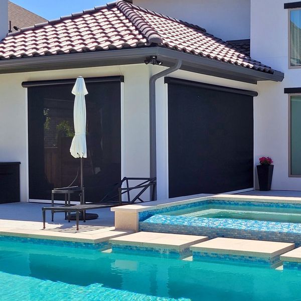 A backyard with a pool in front of a modern house with retractable sun shades. Bright blue sky.