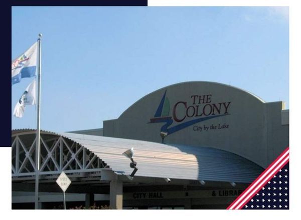 City Hall of The Colony, Texas, under a clear sky, with its logo above the entrance and two flags waving on the left.
