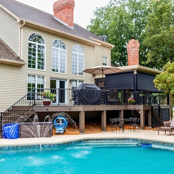 Backyard with a pool, deck, and house. The deck has an outdoor kitchen area, and there's a view of the surrounding trees.