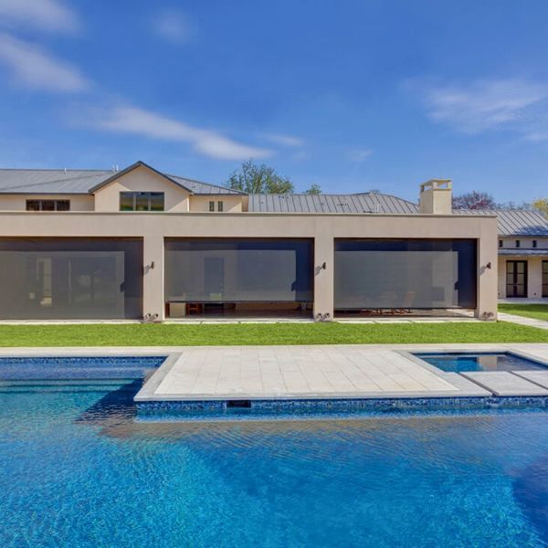 A backyard with a pool in front of a modern house with retractable sun shades. Bright blue sky.