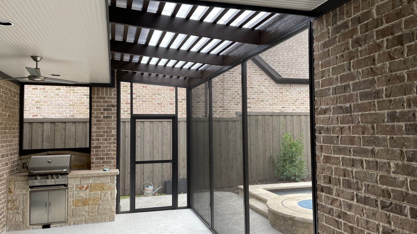 Outdoor kitchen with brick walls, stainless steel grill, stone counter, screened-in area with pergola.