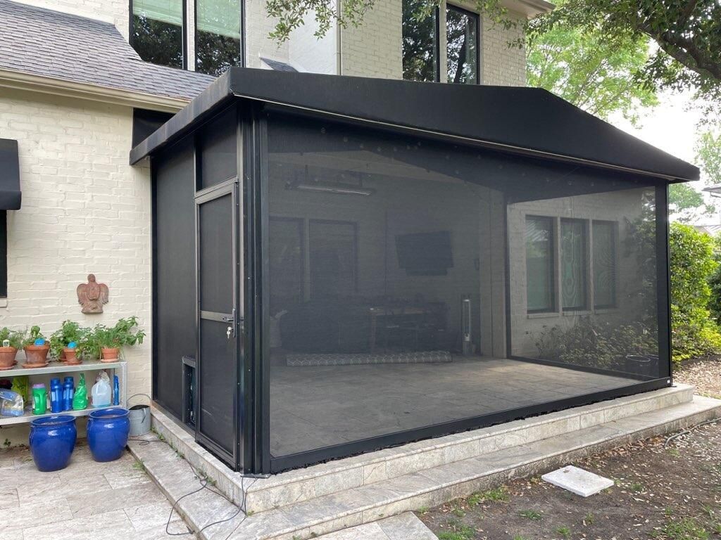 Screened-in patio with black frame, gray concrete floor, and black roof. Includes a door and potted plants.