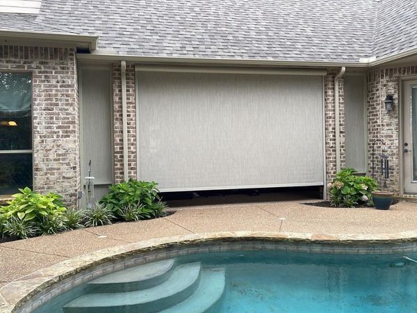 A large, beige retractable sun shade is lowered over an outdoor patio area next to a swimming pool.