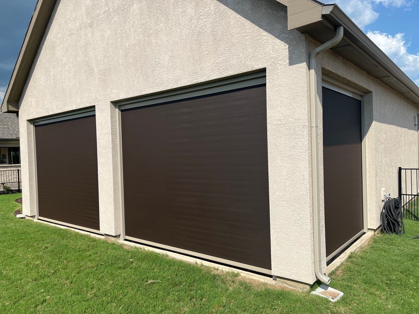 Brown outdoor roller shades on a stucco building next to a grassy lawn.