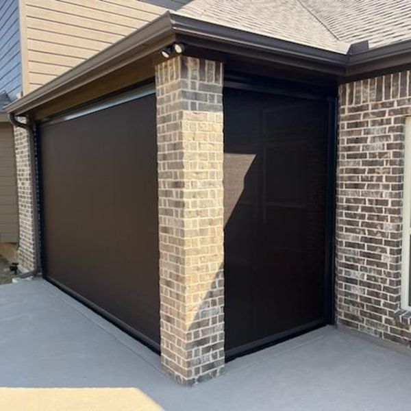 A dark brown exterior shade covers a patio, attached to a brick column and the house.