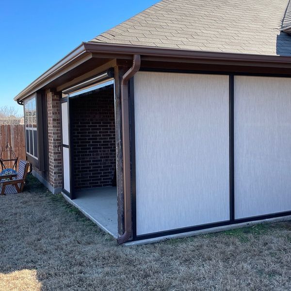 Outdoor patio with brown gutter, white privacy screens, brick wall, and green grass.