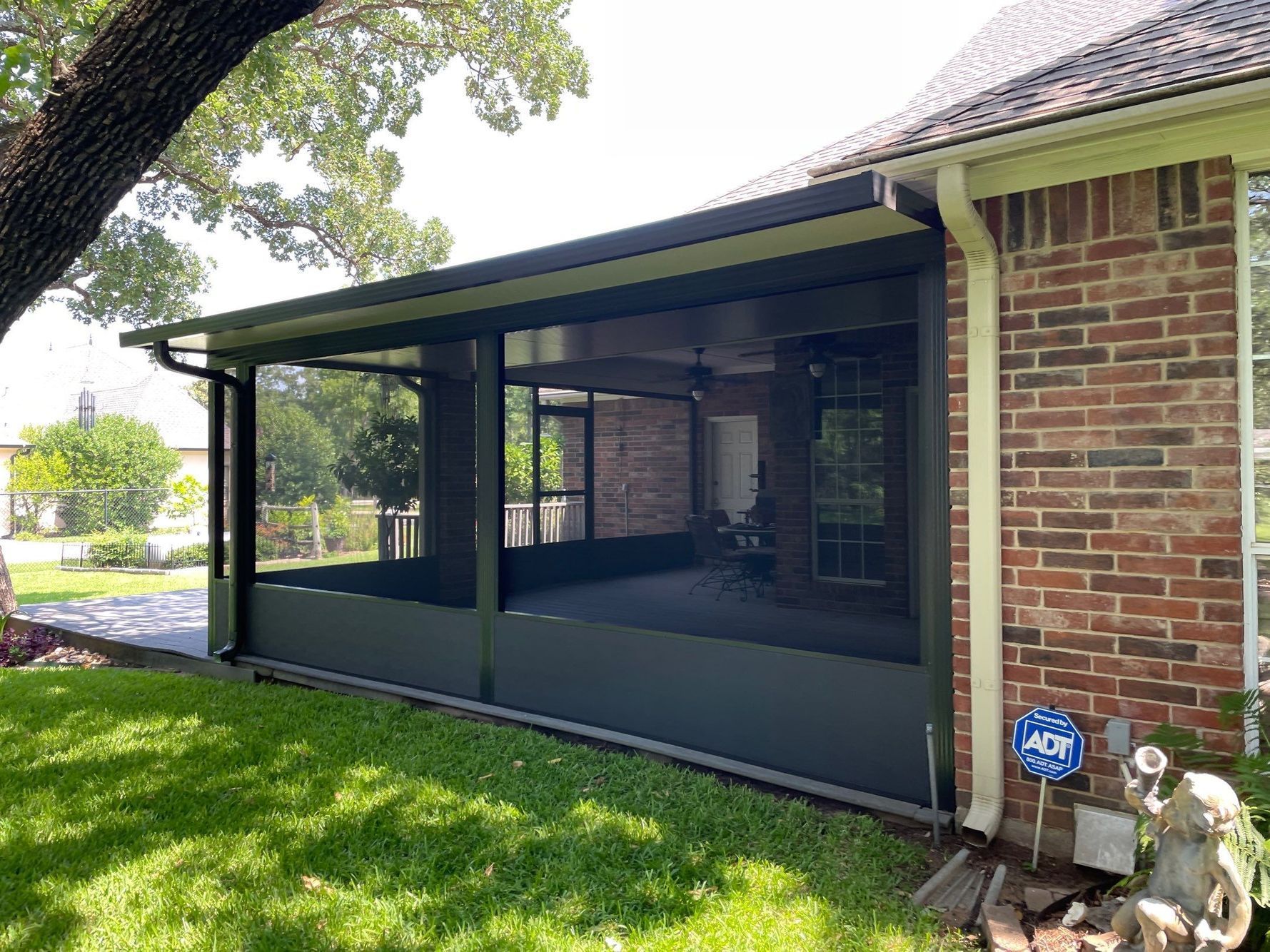 Screened porch with dark screens, attached to a brick house, green lawn in foreground.