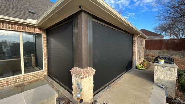 Covered patio with large retractable screens, furniture, and a view of a pool and trees. Black screens are down.