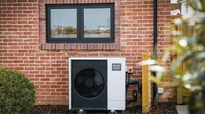 Aerona heat pump outside a kitchen window between a bush and a tree