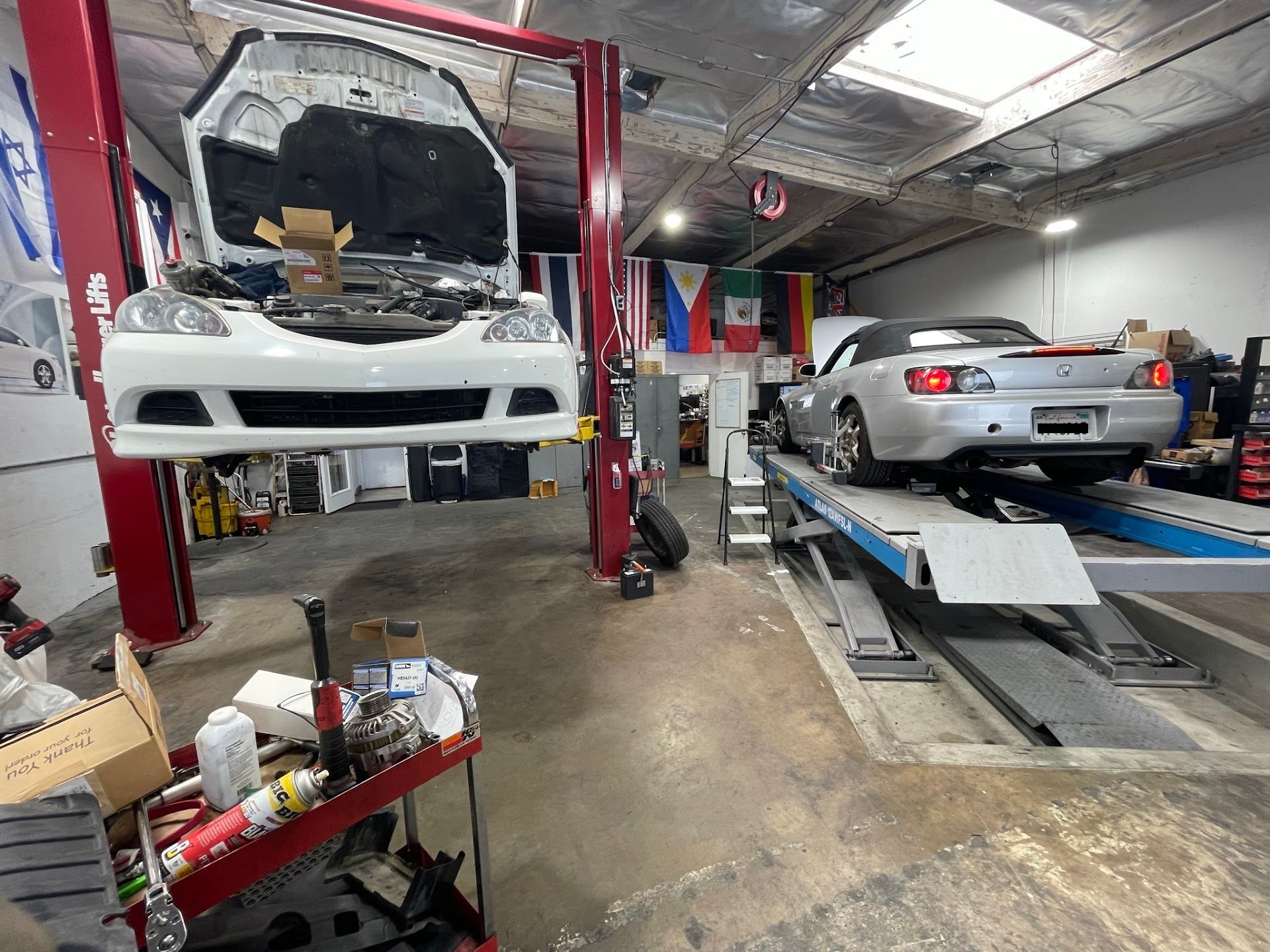 Two cars in a garage, one elevated on a lift with the hood open, another on a ramp | FNP Auto
