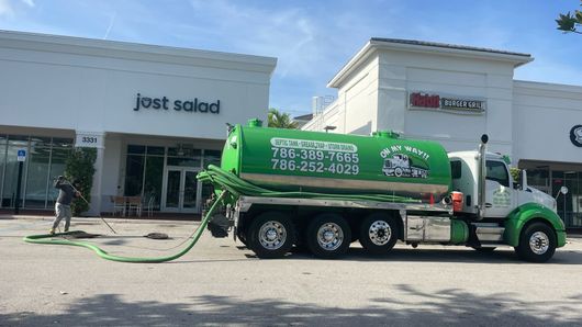 Green vacuum truck parked outside a salad shop and other storefronts in a strip mall
