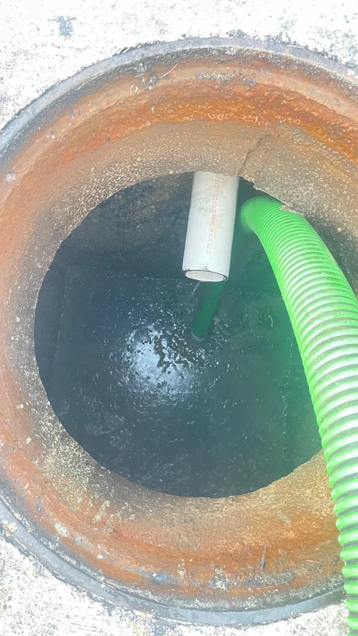 A green hose is being used to pump water into a manhole cover.
