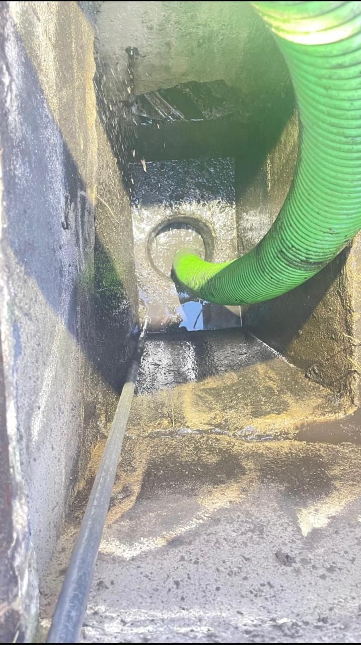 A green hose is being used to clean a drain.