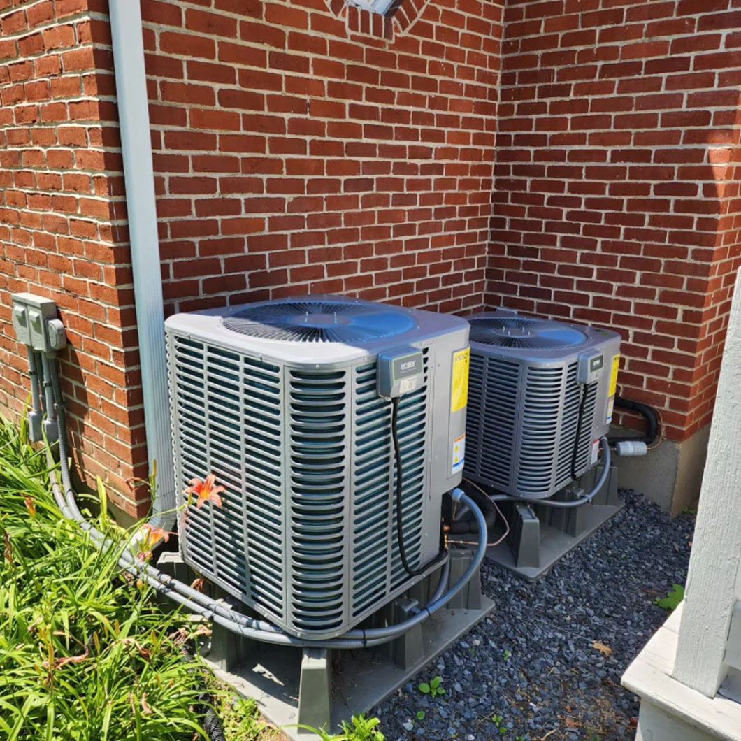 Two air conditioners are sitting outside of a brick building.