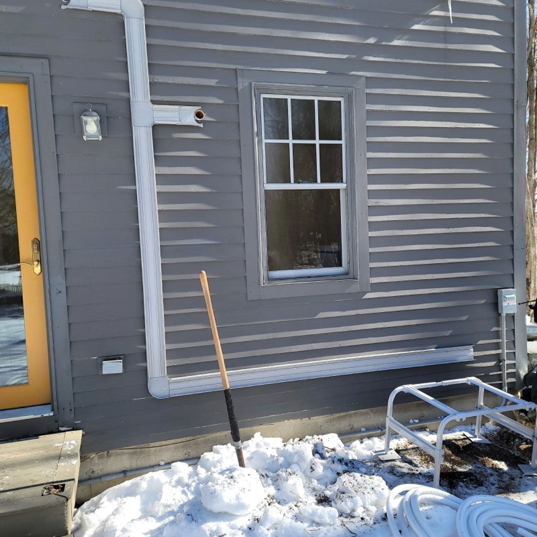 A gray house with a yellow door and a shovel in front of it